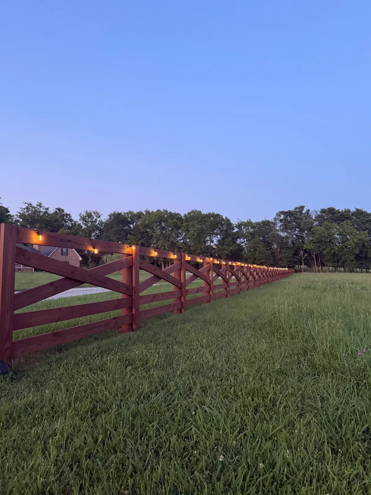 Dark-stained board ranch fence receding into a field at dusk