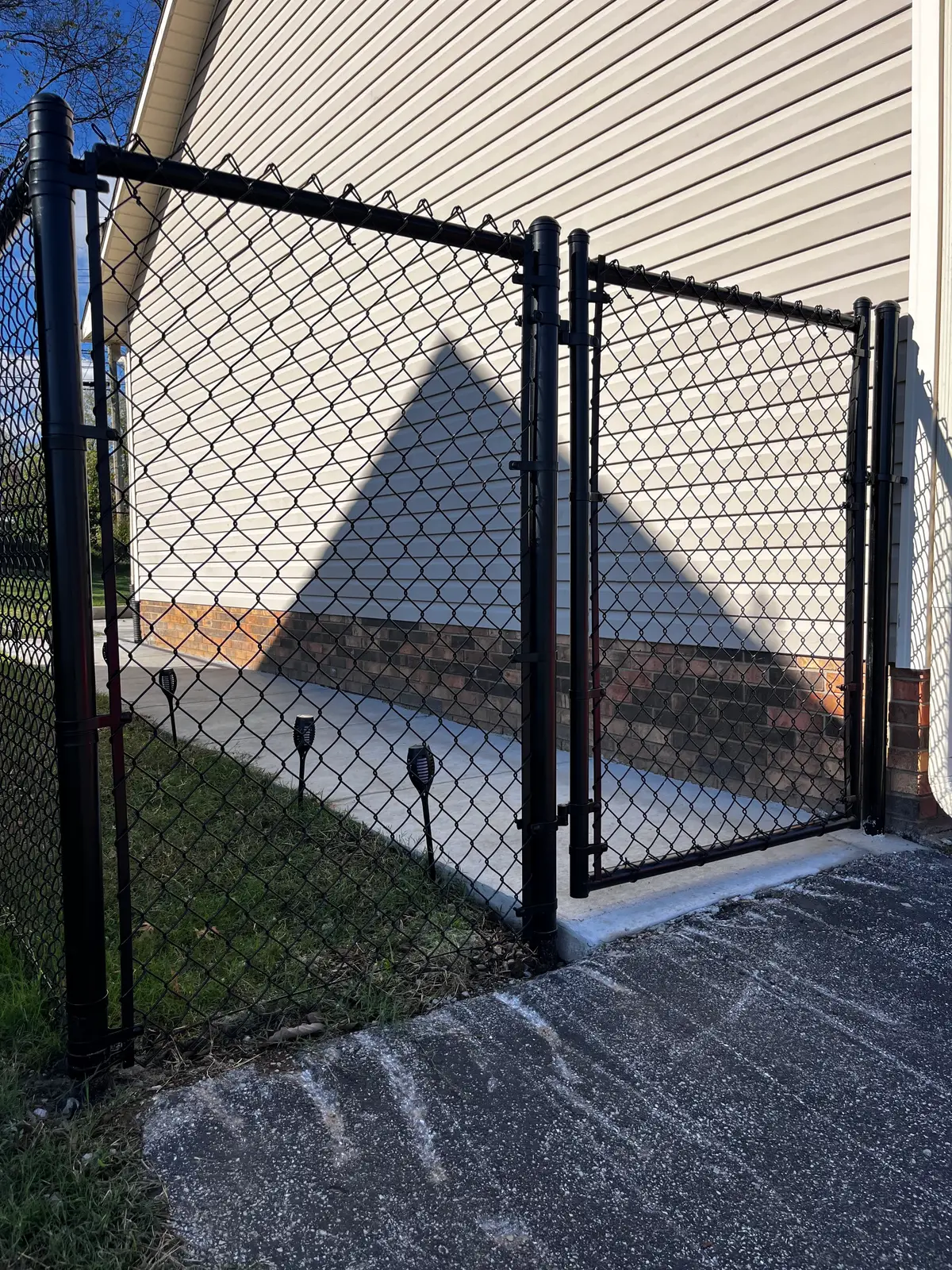 Black metal gate with brick column and chain-link security fence