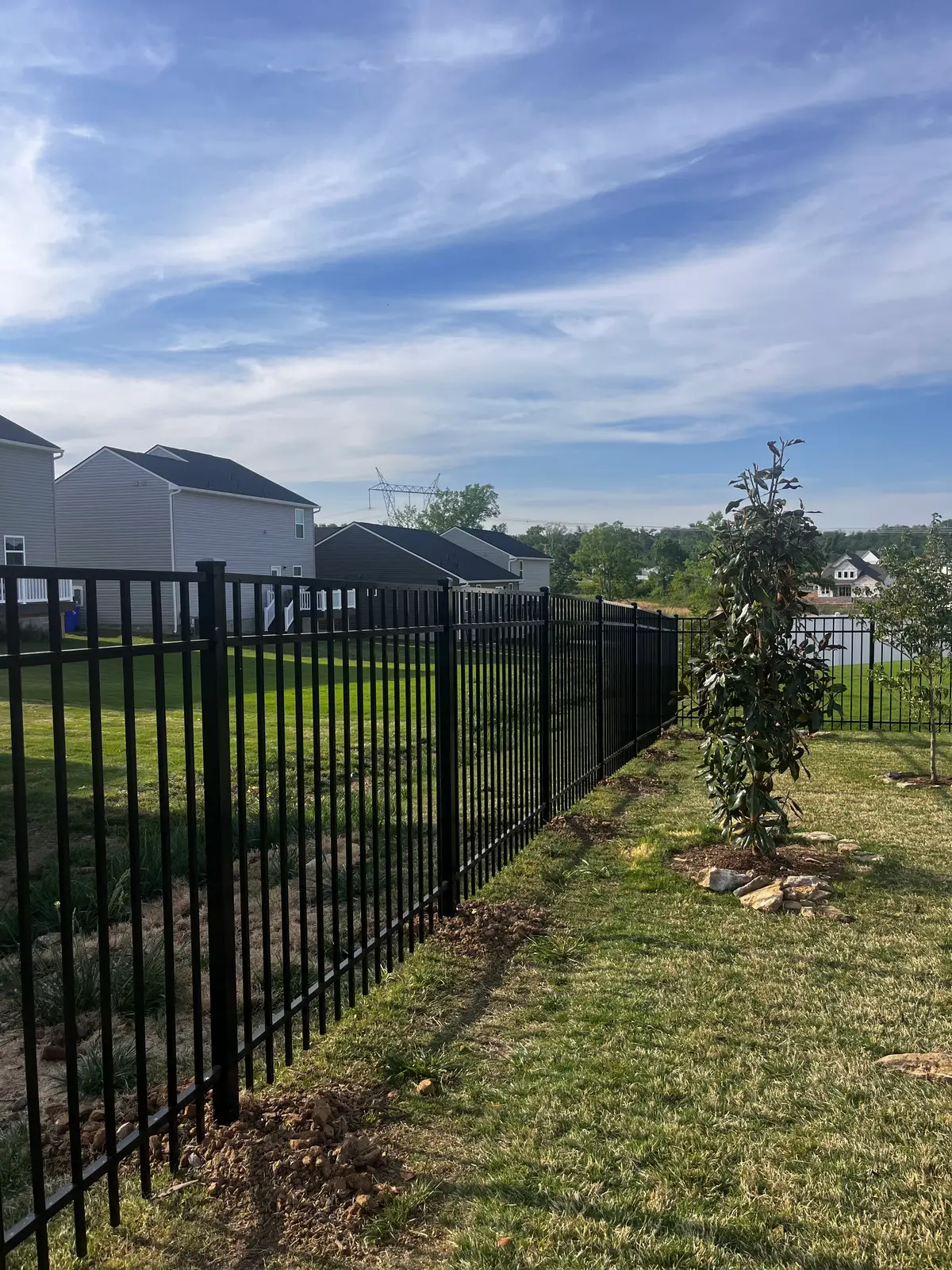 Black double farm gate transitioning into a natural wood board fence