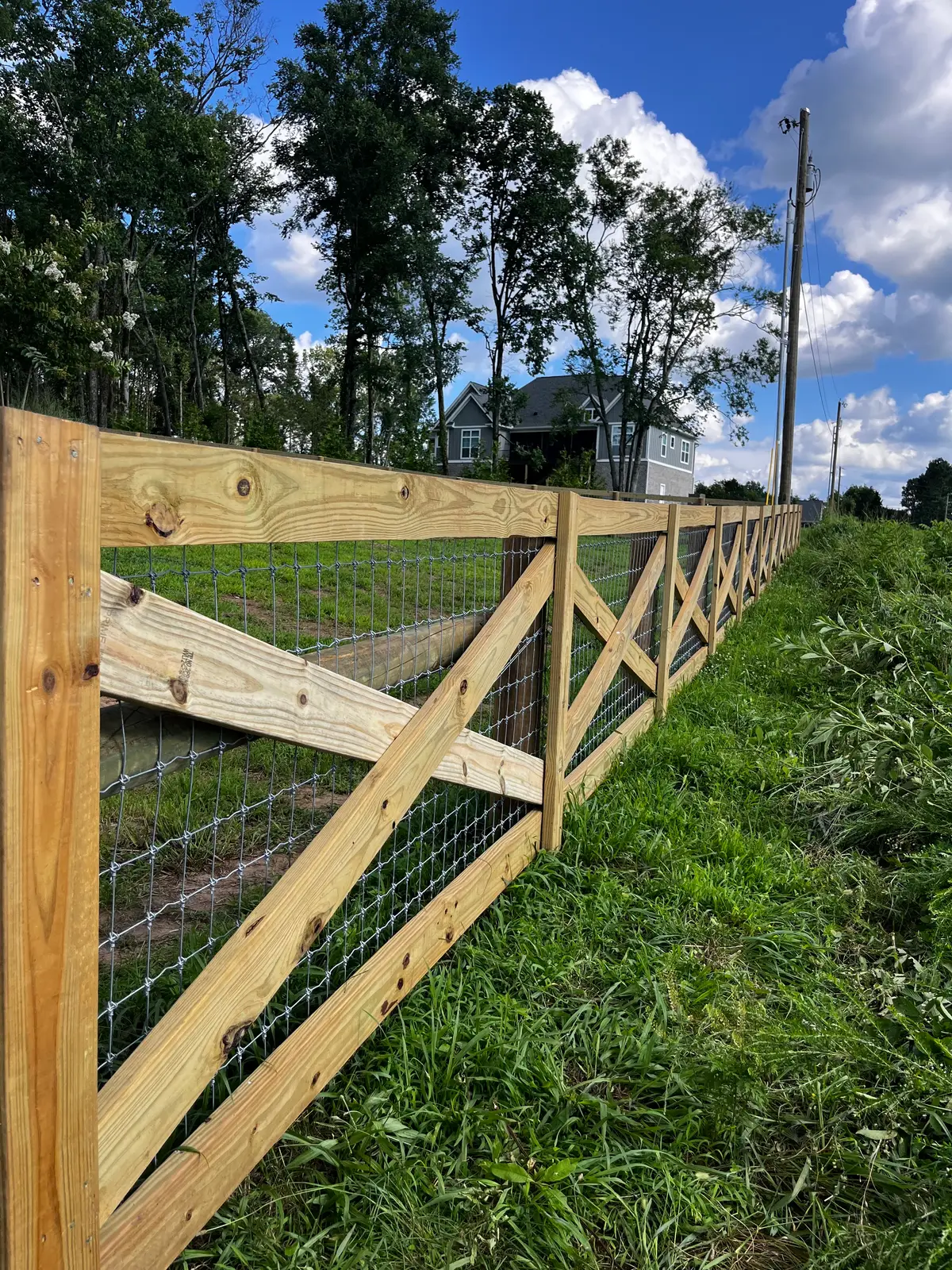 Wood-frame wire fence with cross-brace panels along a pasture