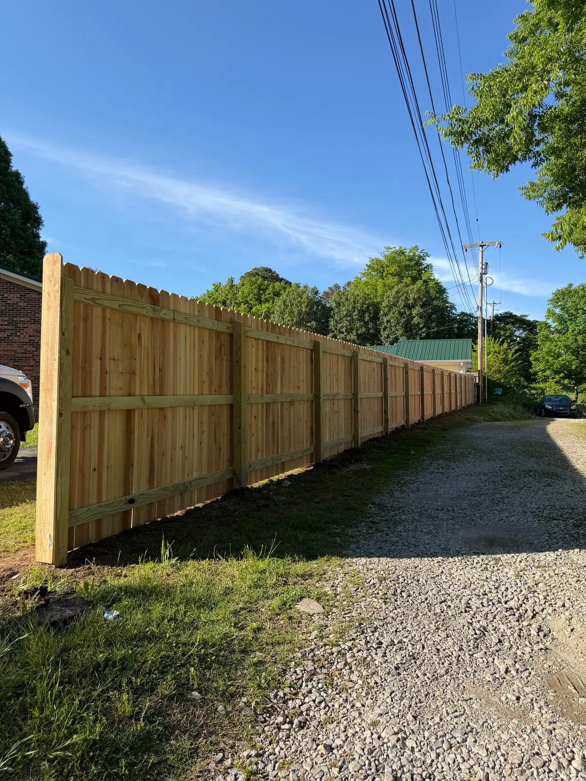 Tall wood privacy fence lining a gravel driveway