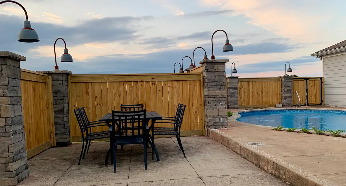 Cedar privacy fence enclosing a pool patio at dusk with string lights